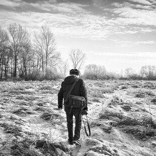 A man walks across a field on a winter's morning with his camera