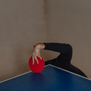 A man holds a table tennis bat in one hand, with the rest of his body hidden under the table