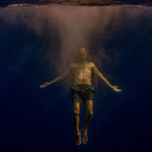 A man swims deep underwater with his arms outstretched 