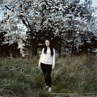 A young woman stands in front of a blossom tree