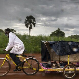 A volunteer community health worker uses his bicycle ambulance to transport a young boy with malaria to the nearest clinic