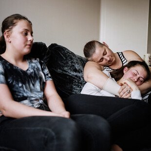 Two teenage girls sit on a sofa with their mother.