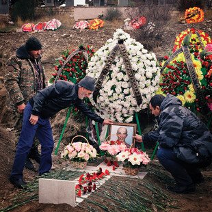 Two men tend a grave covered in flowers. 