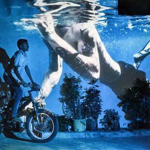 An underwater image is projected behind a man on a motorbike.