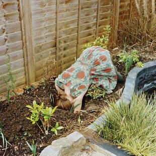 A woman puts her head into a hole in the dirt of her garden. 